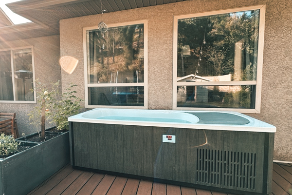 Outdoor hot tub on a wooden deck with large windows in the background