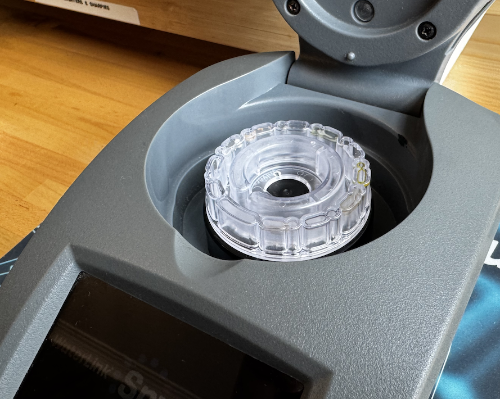 Close-up of a water tester with a clear plastic spin disk on a wooden surface.