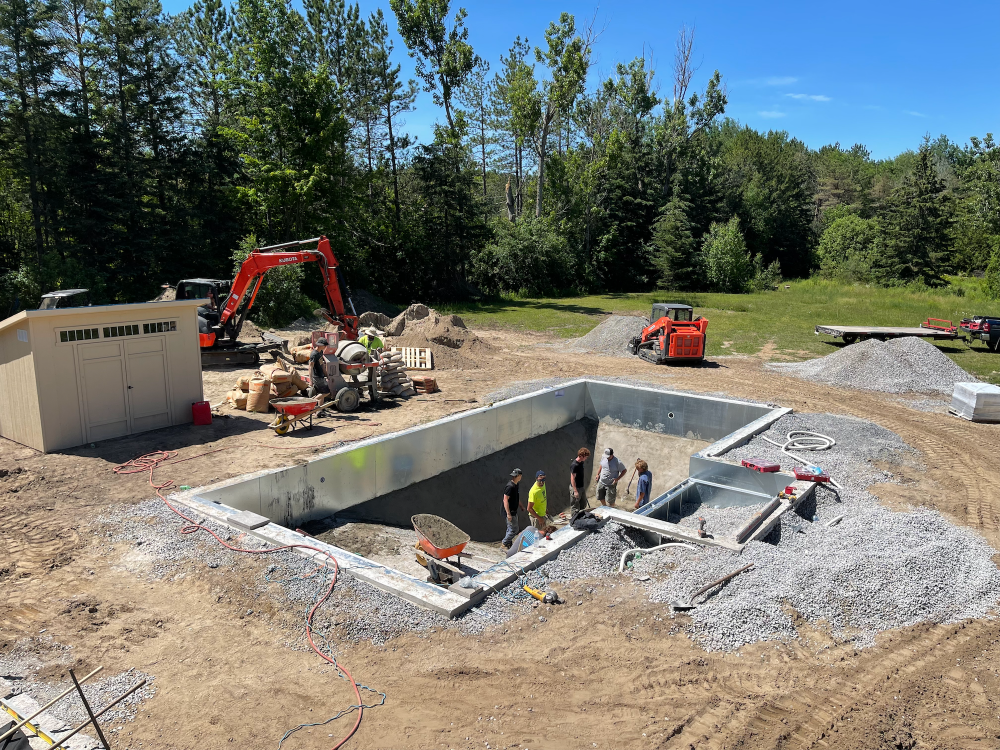 Construction site with a pool foundation and workers in a wooded area