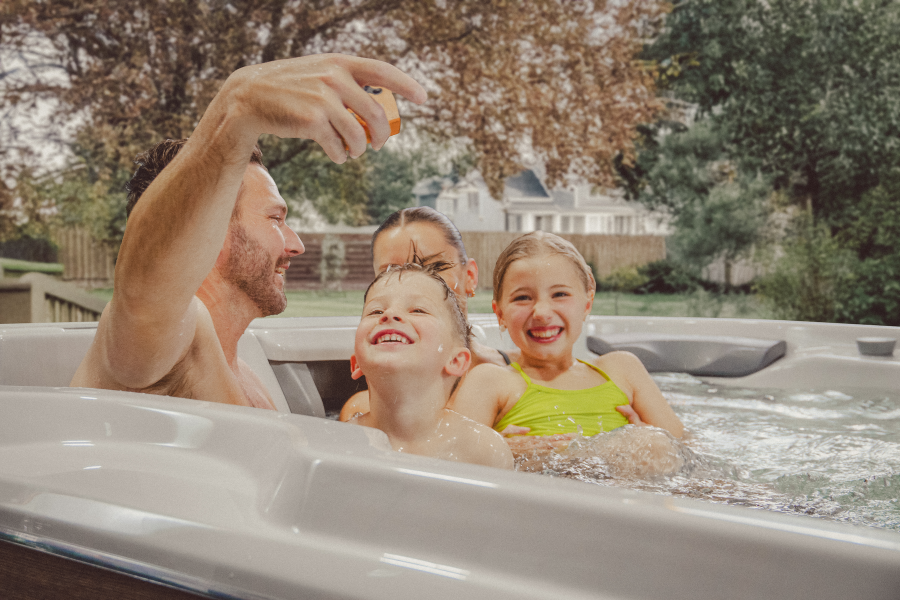 A happy family of four enjoying quality time in the Sundance® Surf™ 17 Swim Spa in a backyard setting.