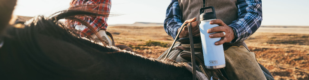 Person holding a YETI water bottle with a horse in a field