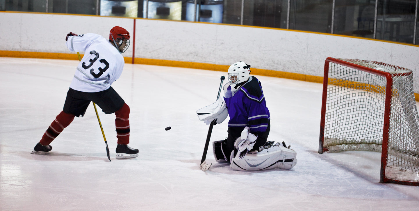 A hockey player takes a shot on a goaltender