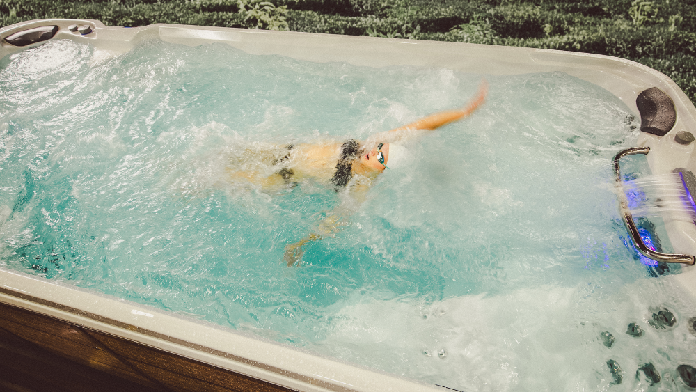 A competitive swimmer using the Sundance® Surf™ 17 Swim Spa with a powerful current in a backyard setting.