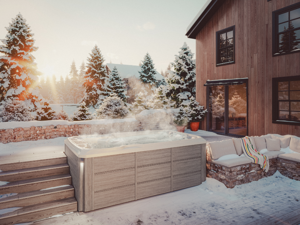 A Sundance® Stream™ 13 Swim Spa steaming in a snow-covered backyard with a wooden house, steps, and outdoor seating under the winter sun.